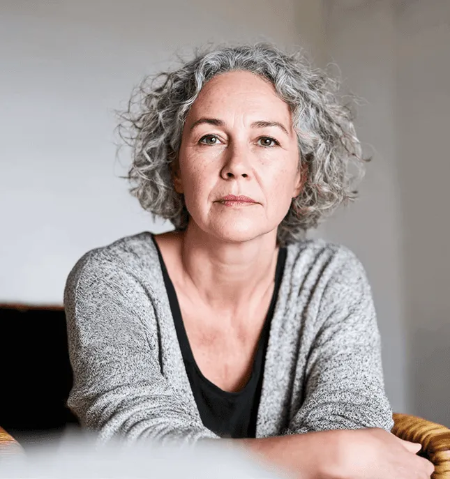 A middle-aged woman with grey curly hair looks calmly into the camera.